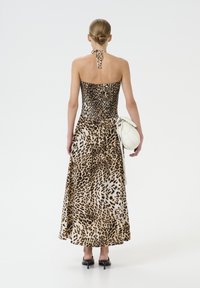 Maxi kjole med leopardmønster, der har et tætsiddende bærestykke og en svajende nederdel. Ryggen har en halterneck og en bundet detalje. Accessoriseret med en hvid taske.