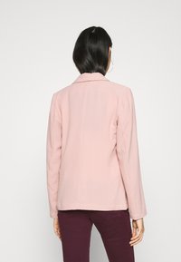 Růžový strukturovaný blazer s límcem a dlouhými rukávy, s jemnou texturou a rovným střihem. Bez viditelných zapínání nebo akcentů.