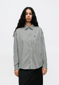 Schwarz-weißer gestreifter Hemd mit Button-Down-Kragen, langen Ärmeln und einer Brusttasche. Der Stoff hat eine glatte Textur.