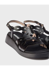 Sandalias negras con un diseño de tira decorativa texturizada. Presentan una plantilla acolchada y una suela plataforma baja y gruesa. Correa ajustable en el tobillo.