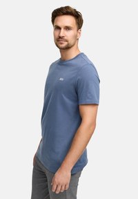 T-shirt di cotone azzurro chiaro con colletto rotondo, maniche corte e un piccolo logo bianco sul petto. Texture liscia e vestibilità casual.
