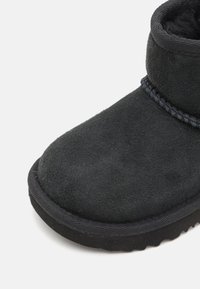 Bottine en suède noir avec une surface texturée, dotée d'un bout arrondi, de coutures décoratives et d'une semelle en caoutchouc.