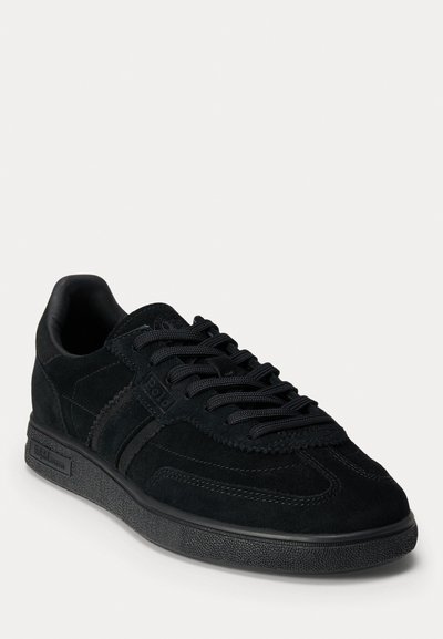 Sneaker nera in suede con lacci frontali, strisce laterali testurizzate, collare imbottito e suola in gomma piatta. Design minimalista con accenti tonali.