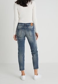 Siniset farkut, joissa on slim fit -leikkaus, kevyesti haalistunut pinta, kaksi takataskua ja ruskea nahkainen etiketti vyötäröllä. Yhdistetty valkoiseen neuleeseen.