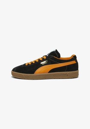 Baskets basses Puma en daim noir avec des bandes et lacets orange, semelle en gomme, et logo Puma Delphin blanc sur le côté.