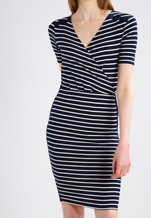 Femme portant une robe rayée horizontale bleu marine et blanche, longueur genou, manches courtes et décolleté en V.
