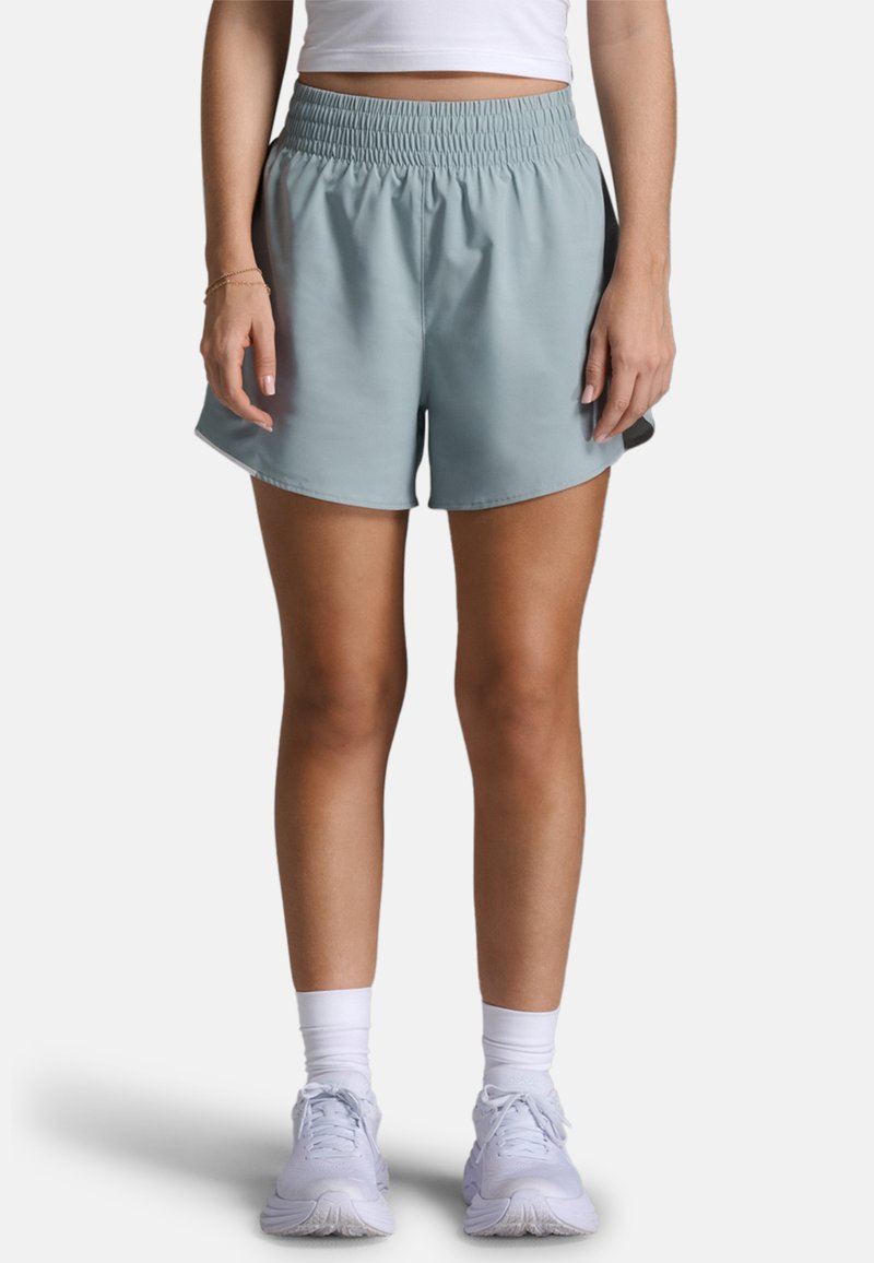 Světlé modré pružné sportovní šortky s elastickým pasem a bočními rozparky, doplněné o bílé boty a ponožky. Hladká textura.