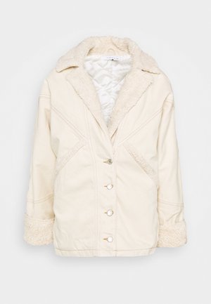 Chaqueta color crema con un cuello y puños esponjosos, que presenta una botonadura frontal, dos bolsillos laterales y detalles de costuras diagonales. Textura suave.