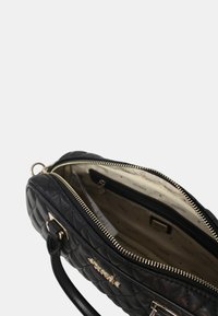 Sort quiltet håndtaske med guldtonet hardware, lynlåslukning og et rummeligt foring indre med en sidelomme. Justerbar strop inkluderet.
