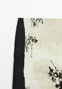 Tissu froissé avec une large bordure noire à gauche et des motifs floraux noirs en coups de pinceau sur fond crème.