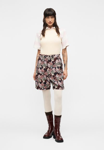 Φλοράλ σορτς σε σκούρους τόνους με μοτίβα σε ροζ, μπλε και πράσινο; συνδυασμένα με ανοιχτόχρωμο εφαρμοστό τοπ και μπεζ καλσόν. Γυαλιστερές καφέ μπότες.