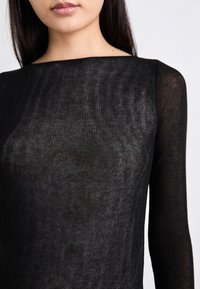 Haut noir à manches longues en tissu tricoté transparent avec un col rond et une finition légèrement texturée. Design simple sans motifs visibles.