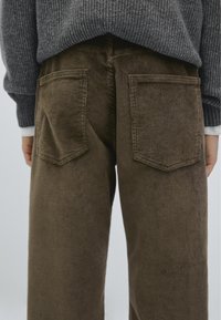 Brune fløjl brede bukser med to baglommer, struktureret ribkonstruktion og høj talje, parret med en grå strikket sweater.