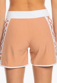 Persikofärgade shorts med vit midja, som har rutiga mönster i vitt på sidorna och en smidig, elastisk tygkänsla.