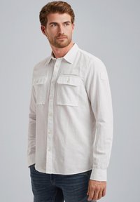 Camisa blanca de manga larga hecha de una tela ligera, con dos bolsillos en el pecho, cierre de botones y un cuello con solapa.