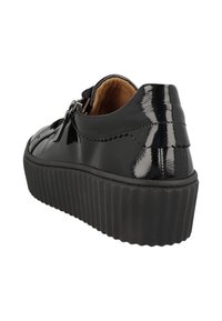 Chaussure en cuir verni noir avec une semelle en caoutchouc noir texturé, présentant un bout rond et un bord festonné décoratif au niveau du talon.