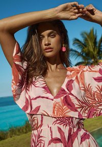 Rochie cu model floral în roz deschis, cu frunze roșu închis și portocalii, decolteu adânc în V, mâneci fluide și detalii la talie.