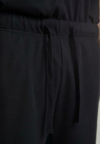 Jogging noir à côtes avec taille élastique, cordon de serrage et tissu texturé. La vue rapprochée met en avant le matériau et les détails de conception.