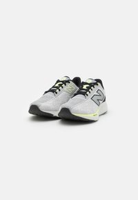 Zapatillas deportivas de malla gris con acentos negros, que presentan una superficie texturizada, detalles reflectantes y una suela semitransparente.