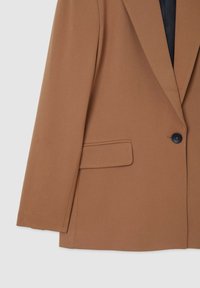 Blazer marron en tissu texturé, avec une fermeture à un bouton, des revers crantés et une poche latérale, doublé en noir.