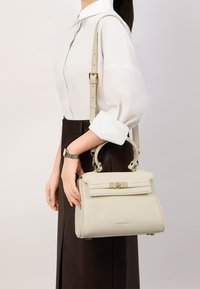 Borsa a tracolla in pelle beige chiaro con forma strutturata, manico superiore e tracolla regolabile. Presenta un pattina e una chiusura metallica con dettaglio del logo.