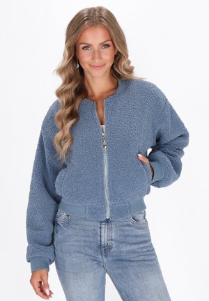 Sininen vetoketjullinen bomber-takki, joka on valmistettu teksturoidusta fleece-materiaalista. Varustettu pyöreällä kaula-aukolta ja sivutaskuilla. Rentoa istuvuutta.