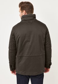 Dunkelgrüne, isolierte Jacke mit hohem Kragen und Knopfmanschetten. Verfügt über ein weiches, strukturiertes Innenfutter und sichtbare Nähte.
