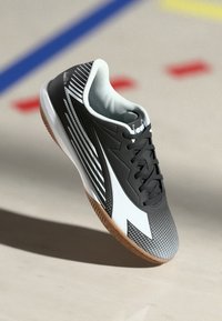 Black and gray athletic shoe features a mesh upper, rubber sole, and diagonal white stripes, with a textured finish and lace-up design.