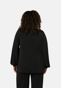 Svart långärmad topp med puffärm och rundad nederkant. Gjord av slätt tyg med en minimalistisk design och utan synliga mönster.