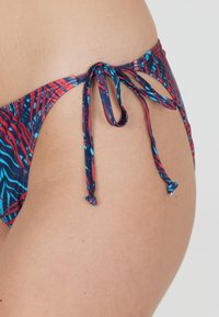 Bikiniunderdel med flerfärgad abstrakt mönstring i rött, blått och svart. Har sidoknutar för justerbarhet och en mjuk textur.