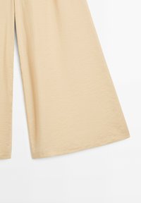 Beiga vida byxor med ett slätt, texturerat tyg. Har hög midja och utsvängd siluett som ger en avslappnad passform.