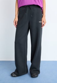 Pantalons de sweat noir avec une coupe décontractée, taille à cordon de serrage et détail de logo à l'avant. Le matériau semble doux avec une texture lisse.