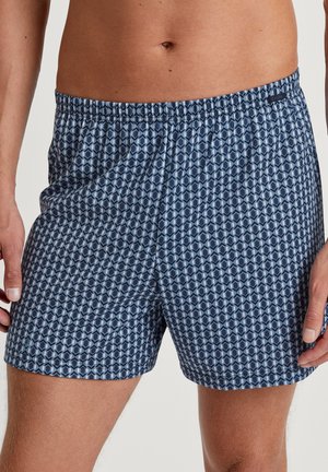 Shorts bleu marine à motif géométrique, avec une taille élastique et un tissu léger. Ils présentent une texture lisse et des poches latérales.