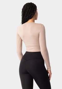 Bežs garām piedurknēm tops ar gludu tekstūru, kombinēts ar augsto jostasvietu melnajām legingām, kas izceļas ar ciešu piegriezumu un smalku izšuvumu detaļām.