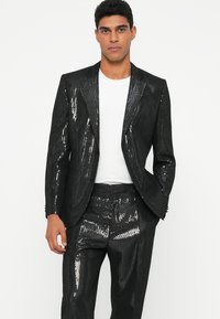 Zwart pailletten kostuum met glanzende textuur en gestructureerde pasvorm, met een blazer met piektoeslag en bijpassende tapered broeken, gedragen over een wit overhemd.