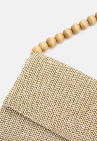 Beige vævet clutch med en struktureret overflade, der har en rem af træperler til bæring. Rektangulær form, minimalistisk design.
