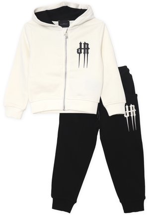 Felpa con cappuccio e zip di colore crema con dettagli neri, abbinata a pantaloni jogger neri con logo coordinato. Realizzata in tessuto morbido e elasticizzato.