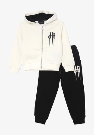 Felpa con cappuccio e zip di colore crema con dettagli neri, abbinata a pantaloni jogger neri con logo coordinato. Realizzata in tessuto morbido e elasticizzato.