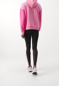 Rosa huvtröja, svarta leggings med detaljer och vita sportskor. Huvtröjan har ett mjukt, texturerat tyg.