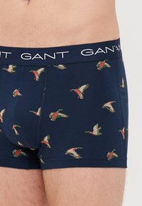 Navy boxer shorts made from cotton, featuring a repeated duck print in green, red, and white. Logo waistband in white.
