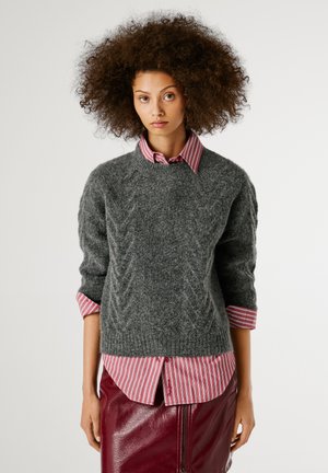 Un pull en tricot gris avec un motif texturé, associé à une chemise à col rayée rouge et blanche et une jupe en cuir bordeaux.