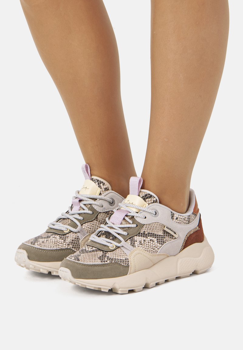 Zapatillas deportivas con un patrón texturizado de piel de serpiente en beige y gris, con una suela acolchada, detalles en lavanda y cordones grises.