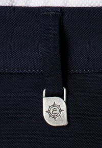 Granatowy materiałowy pas w talii z metalowym zapięciem w kolorze srebrnym, ozdobionym wzorem kompasu oraz grawerowanym logo, charakteryzujący się teksturowaną powierzchnią.