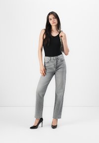 Zwarte mouwloze bodysuit, grijze high-waisted straight-leg jeans, zwarte stilettohakken, met een textuur handtas. Minimalistische achtergrond.