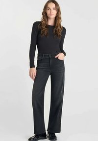 Zwarte top met lange mouwen gecombineerd met hooggetailleerde, wijd uitlopende jeans in donker denim. Heeft een gladde textuur en een klassiek ontwerp met vijf zakken.