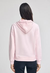 Felpa pink con cappuccio regolabile, polsini a costine e una consistenza morbida, mostrata da dietro. Design semplice senza ulteriori motivi.