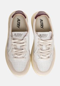 Baskets en cuir blanc avec des accents beige et bordeaux, dotées de détails perforés et de lacets beige. Elles présentent une semelle intérieure douce et texturée ainsi qu'une semelle en caoutchouc.