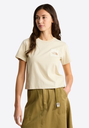 Camiseta de algodón beige con mangas cortas y cuello redondo. Presenta un pequeño logo impreso en el pecho izquierdo en colores suaves. Diseño corto.