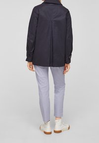 Granatowy płaszcz o średniej długości, z rozporkiem z tyłu, mankietami na guziki i klasycznym kołnierzykiem. Połączony z jasnoszarymi spodniami slim fit i białymi sneakersami.