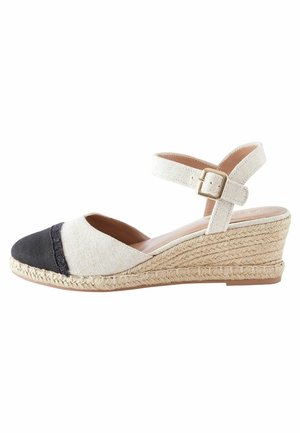 Beige kangasest valmistatud kaldenööriga espadrill, mille must kanvasest esiosa on kaetud. Ülaserv koos ankle strapiga ja klambriga, jõutud jute-keskmise tallaga, tekstuuriga kangas.